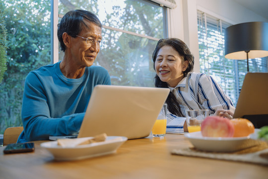 快乐的亚洲老年夫妇在家使用笔记本电脑上网。
