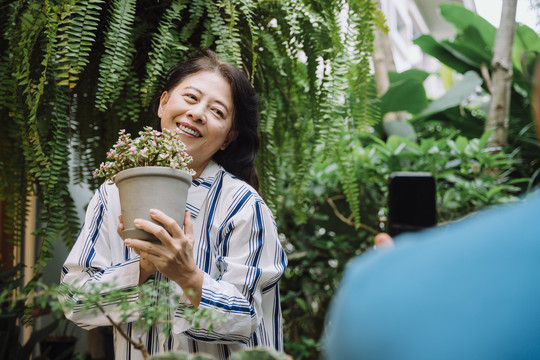 一名男子正在拍摄他妻子在花园里拿着植物的照片。