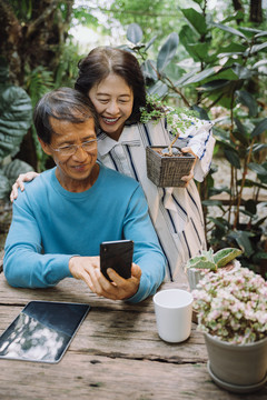 快乐的亚洲老年夫妇在公园用智能手机自拍。