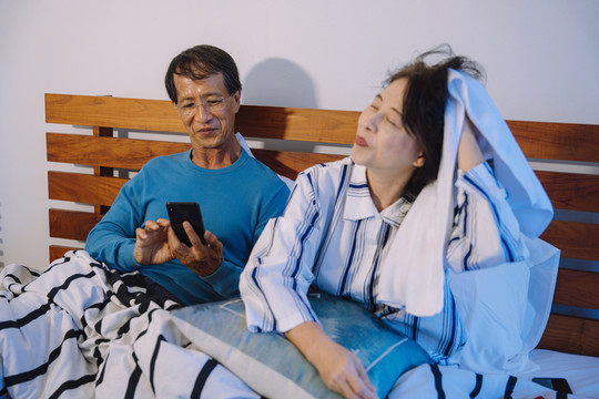 亚洲老年夫妇在卧室里用智能手机和毛巾清洁头发。