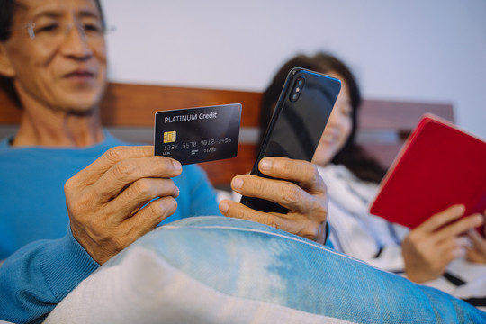 亚洲高级男子用信用卡在智能手机上进行网上购物。