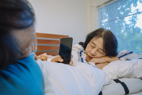 一位老人在床上用智能手机给妻子拍照。