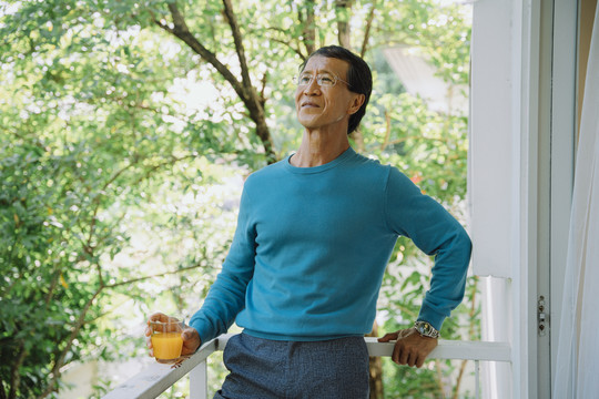 在公园里穿着蓝色毛衣拿着橙汁的亚洲老人的肖像。