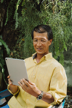穿着黄色t恤的亚洲老人在公园里使用数字笔记本电脑。