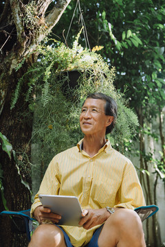 穿着黄色t恤的亚洲老人在公园里使用数字笔记本电脑。