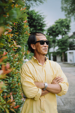 站在植物墙旁戴墨镜的亚洲老人的肖像。