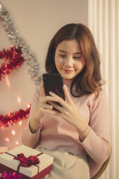 美丽的亚洲年轻女子在圣诞派对上快乐地玩着智能手机。
