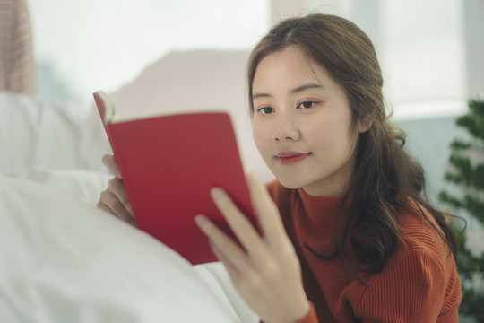 美丽的亚洲年轻女子黑头发在卧室读红皮书。