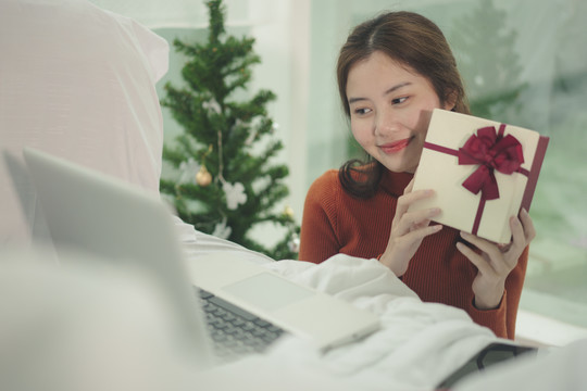 美丽的亚洲年轻女子黑头发在家里用笔记本电脑在线庆祝圣诞节。