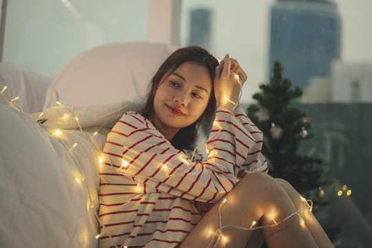 美丽的亚洲年轻女子卧室里挂着圣诞灯，黑色头发。