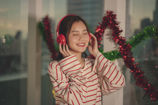 美丽的亚洲年轻女子黑发在圣诞派对上用无线耳机听音乐。