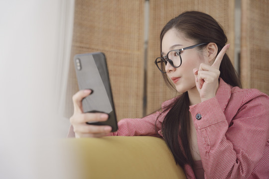 侧视图-年轻的亚洲美女戴着眼镜，通过智能手机观看视频或直播。