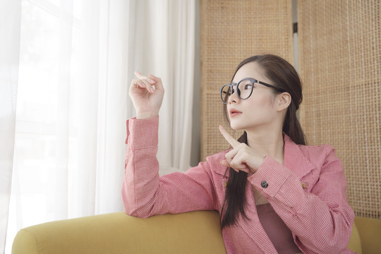 年轻的亚洲美女戴着眼镜，穿着粉色夹克，指着空荡荡的广告空间。