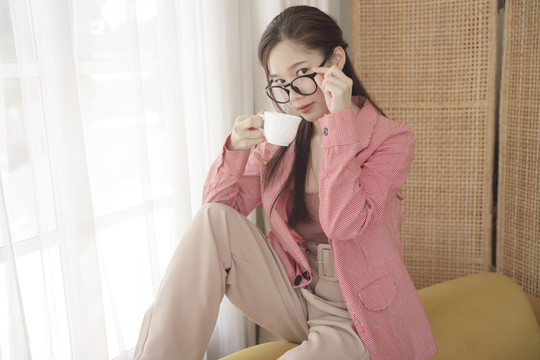 年轻的亚洲美女肖像，穿着粉色夹克，戴着眼镜，享受一杯咖啡。