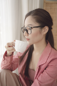 年轻的亚洲美女肖像，穿着粉色夹克，戴着眼镜，享受一杯咖啡。