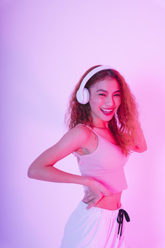 戴着耳机在霓虹灯背景下跳舞的亚洲年轻女子。