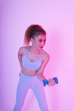健康的亚洲年轻女性在霓虹灯背景下练习哑铃。健身房的概念。