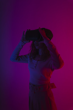 快乐女人在霓虹灯背景下佩戴虚拟现实VR护目镜。