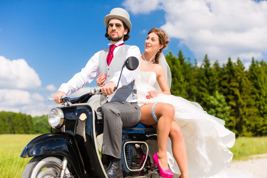 婚礼概念，新娘和新郎骑着摩托车，她正在展示腿上的吊袜带