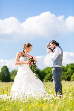 新郎在田野或草地上用相机拍摄新娘