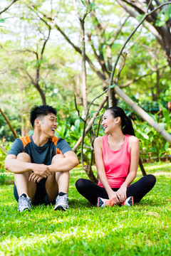 亚裔中国男子和女子在公园健身训练后坐在草坪上