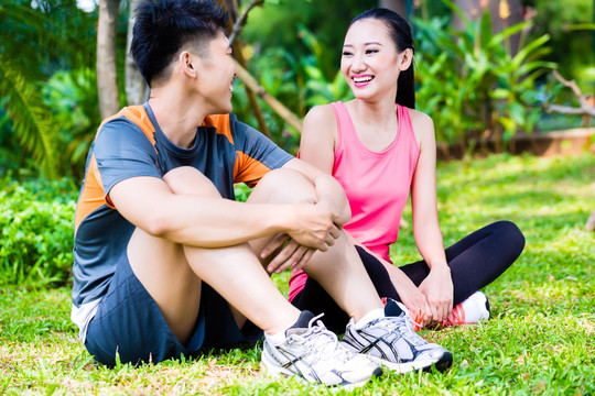 亚裔中国男子和女子在公园健身训练后坐在草坪上