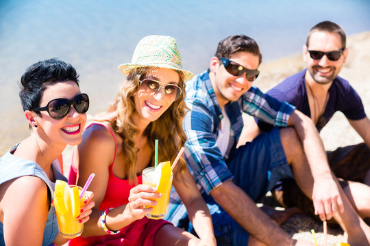 四个朋友坐在湖滩上，在夏日的阳光下喝着鸡尾酒