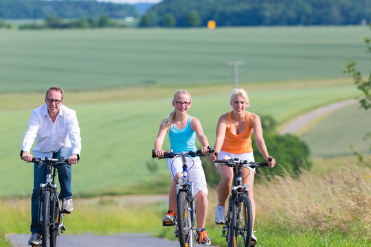 父母和女儿在乡间小路上骑自行车或骑自行车旅游