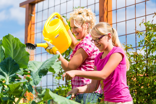 母亲和女儿在花园里用罐子浇灌植物