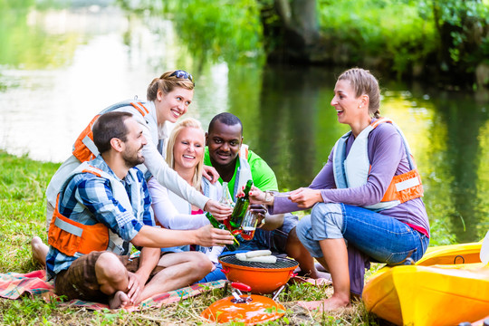 朋友们运动后在森林里烧烤喝啤酒，坐在河边划船