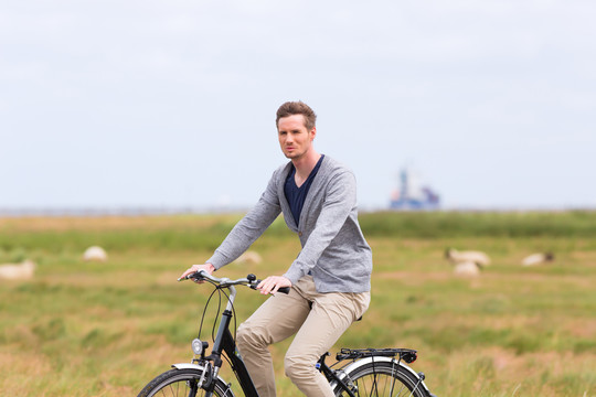 男子骑着自行车在大堤上放羊旅游