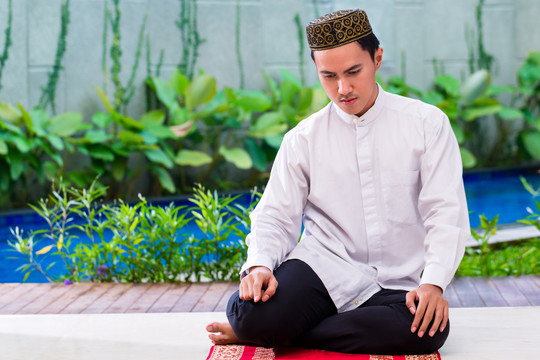 亚洲穆斯林男子穿着传统服装在地毯上祈祷