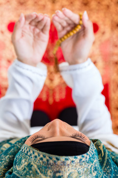 亚洲穆斯林妇女穿着传统服装，戴着珠链在地毯上祈祷