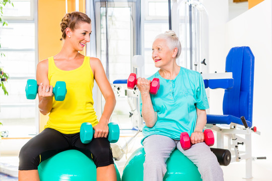 在健身房或健身俱乐部进行哑铃训练的老年和年轻女性