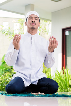 亚洲穆斯林男子坐在热带花园前他家的祈祷地毯上在家祈祷