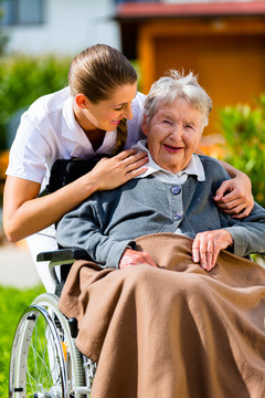 老年妇女在疗养院，护士坐在轮椅上在花园里