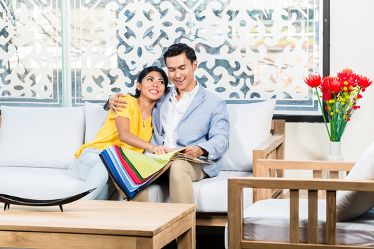 亚洲夫妇在家具店买沙发，坐在沙发上选择颜色和材料