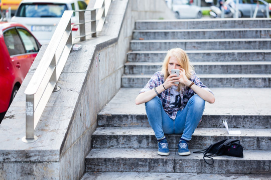 年轻的白人妇女坐在城市户外的楼梯上使用智能手机