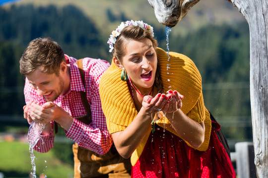 夫妇俩在阿尔卑斯山水源地饮水，场景设置有传统服装