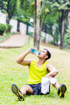亚洲男子在热带公园运动训练后休息，喝瓶装水