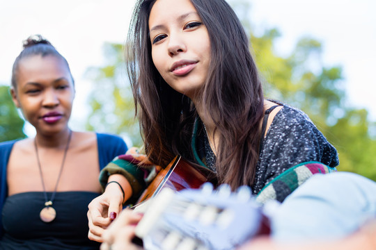 吉他手亚洲女孩与朋友在公园里演奏音乐