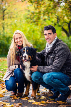 一对夫妇带着小狗在大自然中享受秋天，看着相机