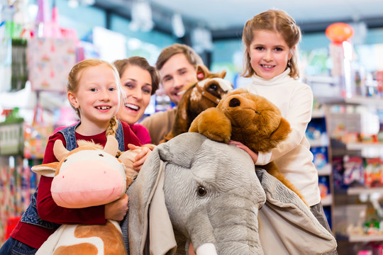 一家人在玩具店里玩填充大象，女孩坐在毛绒玩具上