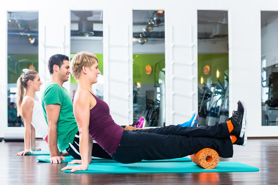 一男两女在健身房或健身俱乐部的地板上做滚动体操