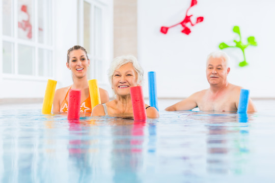 团体或年轻人和老年人在水溶性健身游泳池用泳池面条锻炼
