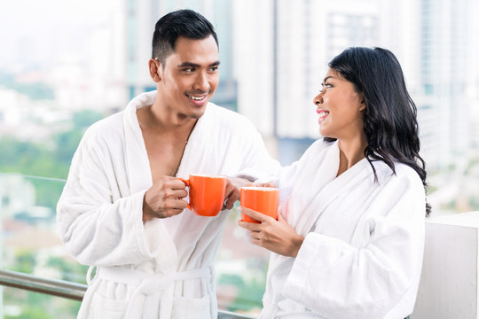 一对亚洲夫妇早上站在城市天际线前，穿着浴衣喝着咖啡