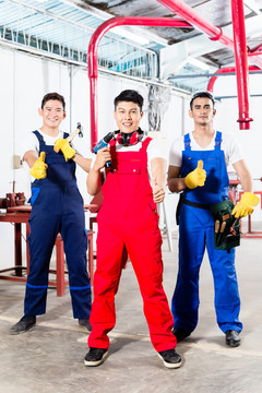 三名亚洲工业工人，一个制造团队，自豪地站在工厂里竖起大拇指