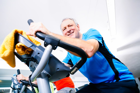 老年人在健身房里骑自行车做运动，看着摄像机