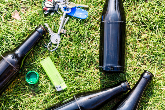 绿色草地上的一个空垃圾桶，酒瓶，打火机和钥匙