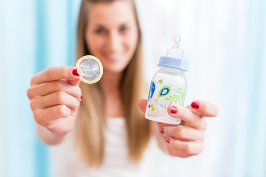 计划生育象征性图片，带避孕套和婴儿奶瓶的年轻女性